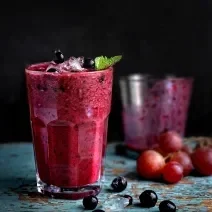 Fotografia em tom escuro de dois copos de vidro, o da frente está cheio com uma bebida de suco de uva com leite e neston, e o do fundo está quase vazio.