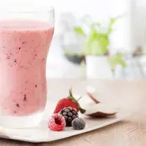 fotografia e tons de rosa e branco de uma bancada bege vista de frente, contém um copo transparente com a bebida de frutas vermelhas e ao lado contém frutas vermelhas.