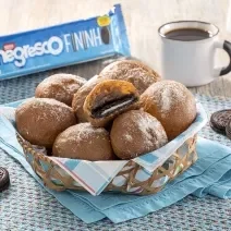 Fotografia mostra uma cestinha com bolinhos de chuva recheado com biscoito. No fundo um pacote de biscoito e uma xícara de café.