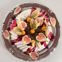 Fotografia em tons de rosa com uma sobremesa decorada com figo e pitaya ao centro. A sobremesa é um pavlova tropical feito com geleia de pitaya