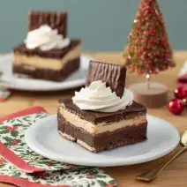 Foto da receita de Mini Ópera Cake, em um prato branco, sobre uma bancada de madeira decorada com itens natalinos e uma colher dourada