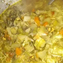 Fotografia de uma panela de alumínio grande com uma sopa de legumes variados.