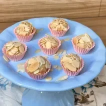 Fotografia em tons de azul e rosa com um prato azul ao centro. Em cima do prato, existe 7 brigadeiros de caramelo salgado cobertos com amêndoas laminadas.