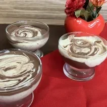 Fotografia de três recipientes com mousse de maracujá com creme de nescau mesclado. Os recipientes estão sobre um pano vermelho e um pano marrom de tom escuro.