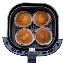 Fotografia vista de cima de quatro muffins de banana sem glúten dentro da cestinha da air fryer, a qual está sobre um fundo branco.