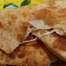 Fotografia de alguns pasteis com creme de calabresa e banana d'água, um sobre o outro. O pastel de cima está cortado na metade com queijo escorrendo.