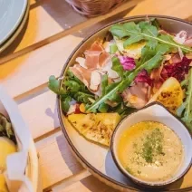 Fotografia de dois recipientes fundos de vidro com salada de abacaxi deliciosa feita com abacaxi, batata, presunto, uva-passa e um molho para acompanhar, no mesmo recipiente.