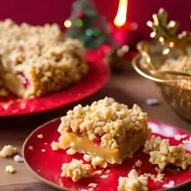 Receita de Cuca Natalina da Vó Rosa, tradicional e deliciosa, feita com uma massa à base de nata e farinha, com frutas cristalizadas e finalizada com uma farofa doce crocante, servida em uma mesa de natal sobre um prato vermelho