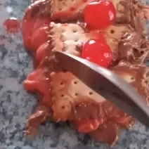 Fotografia em tons de rosa com vários biscoitos Choco Trio recheados com creme de brigadeiro com cerejas. Ao topo da sobremesa existe 3 cerejas inteiras