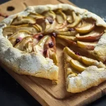 Fotografia em tons de marrom com uma tábua de madeira ao centro. Em cima da tábua existe uma torta rústica de maçã com a massa feita de NESTLÉ Farinha de aveia.