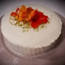 Fotografia em tons de branco em uma bancada de madeira de cor branca. Ao centro, um prato rosa contendo o bolo.