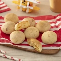 Fotografia em tons de vermelho com vários pães de queijo feitos com NINHO Primeira Infância ao centro.