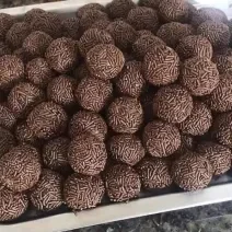 Fotografia de vários brigadeiros de café passados no granulado tradicional. Os brigadeiros estão dentro de uma forma grande retangular de alumínio.