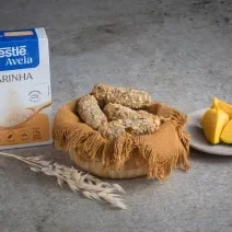 Foto receita de Croquete Vegetariano, servidos em uma cesta de vime, sobre uma bancada de mármore onde há uma caixa de nestlé farinha de aveia à esquerda e pedaços de abóbora sobre um prato à direita além de um ramo de trigo à frente