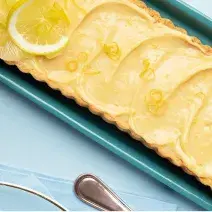 fotografia e tons de azul e amarelo tirada de cima de uma bandeja azul com a torta e rodelas de limão por cima