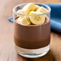 Foto da Receita de Mousse Chocolate com Banana. Observa-se um copo com o mousse dentro e bananas decorando o topo. Imagem ilustrativa gerada por inteligência artificial.