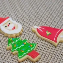 Fotografia de três biscoitos de gengibre em formatos diferentes com decorações natalinas, sobre uma mesa de tom claro.