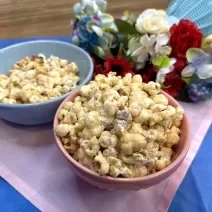 Fotografia em tons de azul e rosa com um potinho rosa e um azul ao centro. Dentro de cada pote existe uma receita de pipoca doce polvilhada com ASCENDA Sem sabor