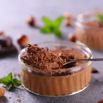 Fotografia em tons de azul com um pote de vidro ao centro. Dentro do pote existe uma mousse de chocolate feita com nescau