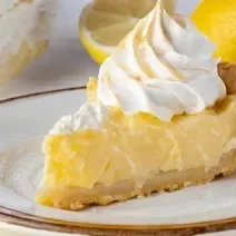 Fotografia de um pedaço de torta de limão com merengue em um prato raso grande.