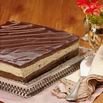 fotografia em tons de marrom de uma bancada marrom vista de frente, em um suporte de alumínio contém a torta com camadas de mousse e chocolate por cima.