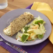 Fotografia em tons de lilás com um prato lilás ao centro e uma toalha amarela. Dentro do prato existe uma receita de wrap com sementes de chia e abóbora recheado com um creme de ricota com Ninho e acompanhado de uma salada.