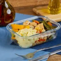 Fotografia de uma marmita retangular pequena com cubos de lombo suíno, abóbora cabotiá e vagem e cenoura ao shoyu. A marmita está sobre dois panos sobrepostos de cor azul, ao lado de talheres e uma mini tábua com pimenta e azeite.