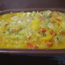 Fotografia de uma moqueca de ovo e mamão verde dentro de um recipiente escuro.