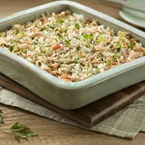 Foto de uma fôrma verde com arroz cremoso dentro em cima de uma tábua de madeira e um pano branco