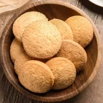 Imagem de pequenos biscoitinhos dispostos sobre um prato fundo de madeira, tons de dourado, amarelo e marrom.