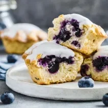 Fotografia em tons de branco com três bolinhos cupcakes ao centro. Os cupcakes são feitos com blueberries e cobertura de limão.