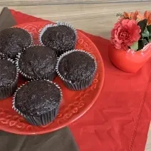 Fotografia em tons de marrom com vermelho com um prato vermelho ao centro. Em cima do prato existe vários muffins feitos de banana, aveia e nescau