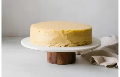 Fotografia de um bolo de maracujá com mousse de maracujá espalhado por todo o bolo, que está em um prato branco, sobre um apoio de madeira.