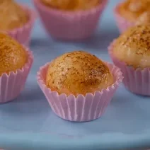 Fotografia de seis unidades de embalagens rosas, uma perto da outra, formando um hexágono. em cada forminha, tem um brigadeiro de creme brulée. As embalagens estão sobre um apoio de cor azul claro.