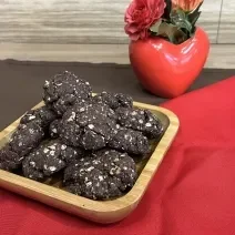 Fotografia em tons de vermelho e marrom com um recipiente de madeira ao centro. Dentro do recipiente existe vários cookies de NESCAU com NESTLÉ Aveia Flocos!