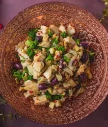 Fotografia vista de cima de uma salada de bacalhau que está dentro de um prato grande de tom mais escuro sobre. 