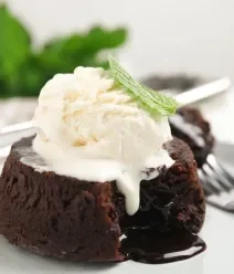 Fotografia de um petit gateau com uma bola de sorvete por cima e uma folha de hortelã, sobre um prato raso e grande.