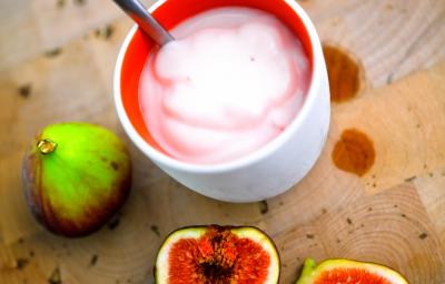 Fotografia de um creme de figo com creme de leite em um recipiente de cerâmica na cor branco e vermelho. Ao redor, dois figos inteiros e mais duas metades do fruto ao lado.