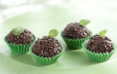 fotografia em tons de verde e marrom, contém 4 brigadeiros com granulados por cima dentro de forminhas verdes e todos tem uma folha de hortelã por cima para decorar