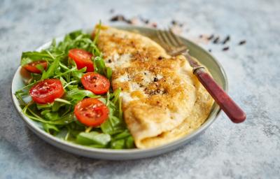 Foto da Receita de Omelete Baveuse. Observa-se um prato com a omelete dobrada no meio, servida com salada de rúcula e tomatinhos cerejas cortados ao meio.