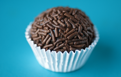 Fotografia de um brigadeiro em uma forminha sobre uma mesa azul.