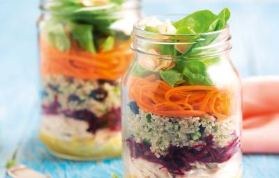 Fotografia em tons de azul em uma bancada de madeira azul, dois potinhos de vidro com a salada de quinoa, beterraba, cenoura e agrião dentro deles. Ao lado, um paninho rosa e dois garfos.