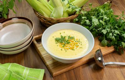 Fotografia em tons de verde com um pote branco ao centro. Dentro do pote existe uma receita de creme de milho.