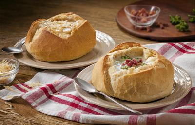 Foto de um pão italiano com sopa creme de queijo dentro e bacon decorando em cima da receita