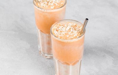 Fotografia de dois copos de vidro com um suco de pitanga com melaço de cana. Dentro dos copos com o suco, um canudo de metal, e embaixo dos copos, uma mesa cinza em tom claro.