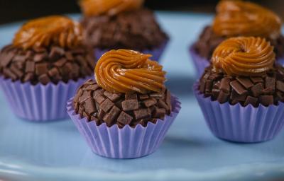 Fotografia de cinco unidades de forminhas azuis com brigadeiro de pão de mel, com doce de leite por cima de cada unidade. Os brigadeiros estão sobre um apoio decorativo de cor azul.