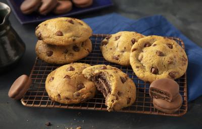 Fotografia em tons de preto e azul de uma bancada preta com um grade dourada, sobre ela cookies. Ao fundo um paninho azul e biscoitos negresco cobertos de chocolate espalhados.