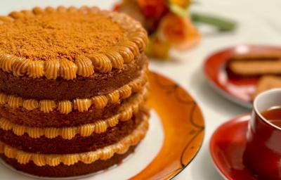 Fotografia em tons de caramelo com um prato de cor marrom ao centro. Em cima do prato existe um bolo com várias camadas de doce de leite e coberto com biscoito triturado