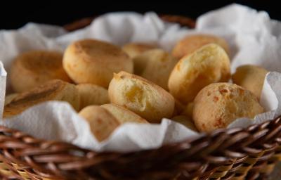 Várias unidades de pães de queijo colocadas dentro de um cesto sobre uma toalha branca.