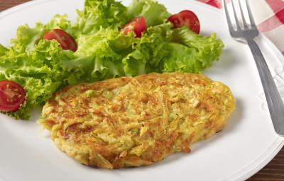 Fotografia em tons de branco, verde e amarelo de um prato branco redondo com folhas de alface com tomate, uma tortilha e um garfo sobre o prato. Ao fundo um paninho xadrez vermelho e branco.